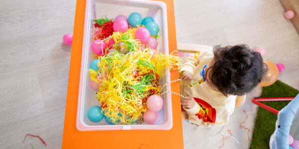 A photo taken from above showing a child playing with a sensory tray full of toys.