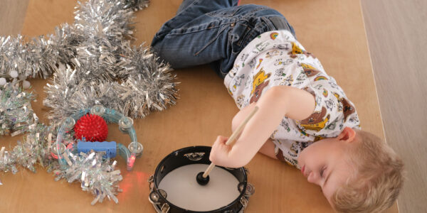 Thomas, a young boy, lying on his side on a resonance board with a tambourine, drumstick and tinsel.
