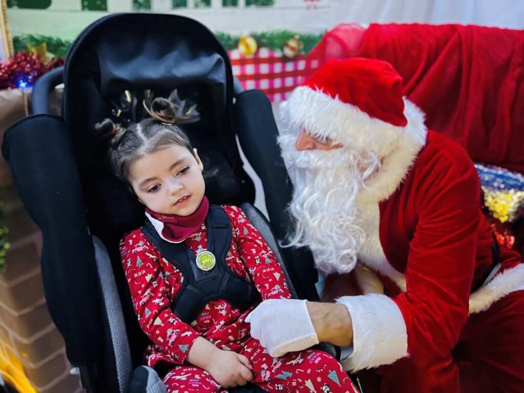 Verity in her wheelchair meeting Santa, who is kneeling beside her.