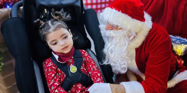 Verity in her wheelchair meeting Santa, who is kneeling beside her.