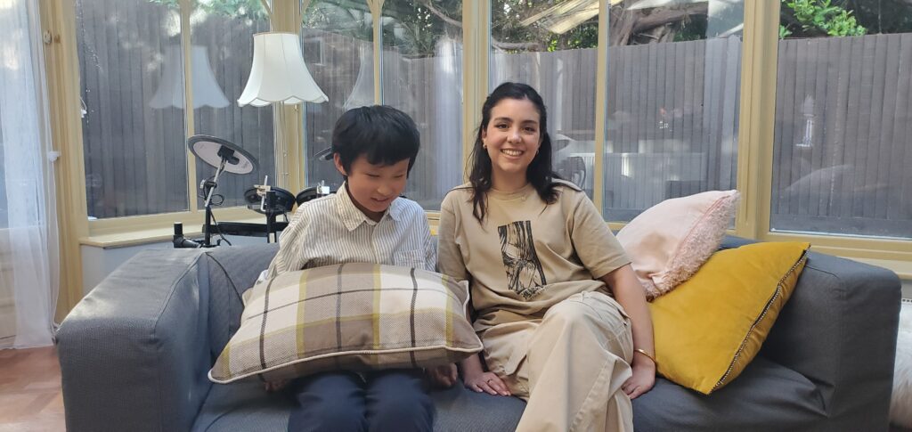 A smiling teenage boy and girl sit side-by-side on a sofa.