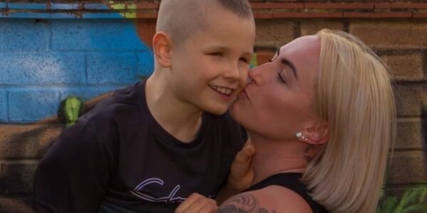 A boy smiles as his mum picks him up for a kiss