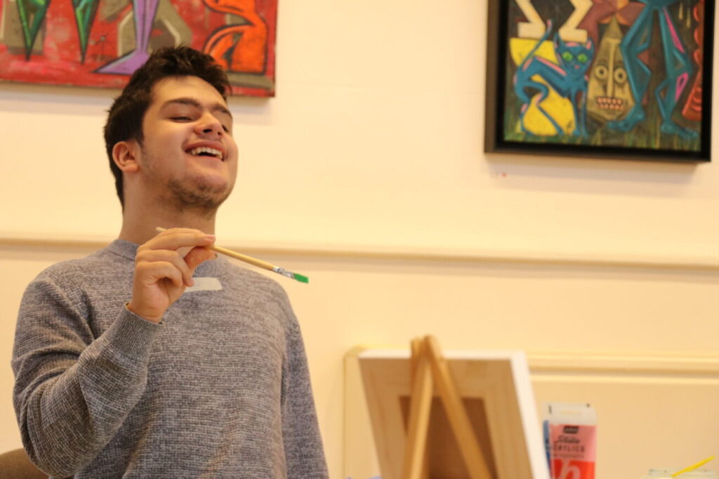 A boy smiles holding a paintbrush