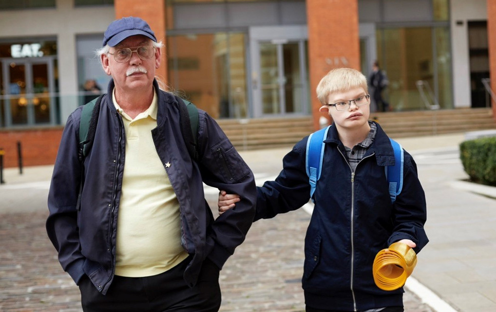 A man in a cap and dark jacket linking arms with his son in dark clothing