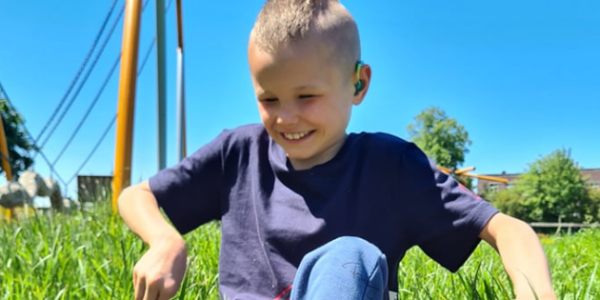 A boy smiles outside as he plays in the grass.