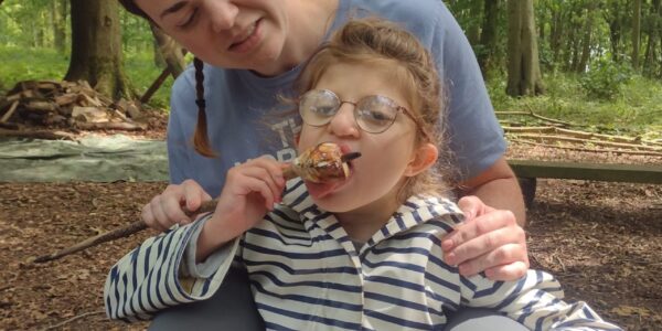 Orla tasting a marshmallow while sitting with a Sense Holidays volunteer in the woods.