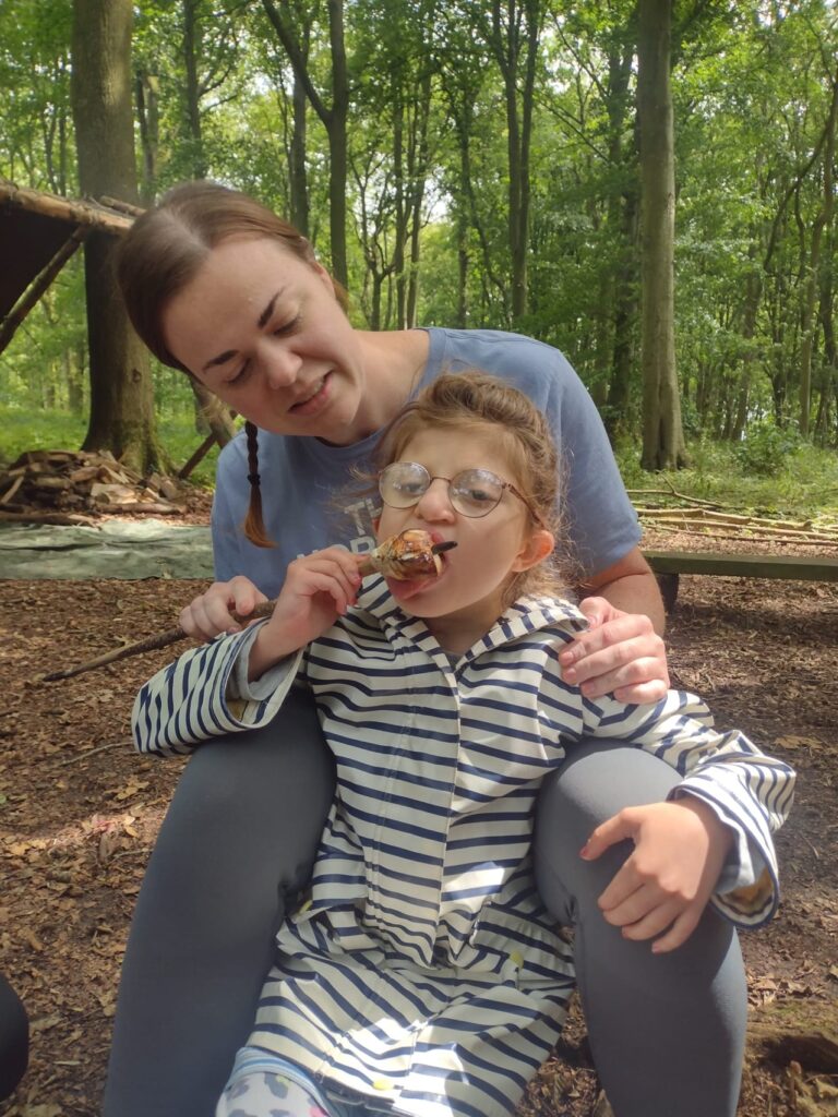 Orla tasting a marshmallow while sitting with a Sense Holidays volunteer in the woods. 
