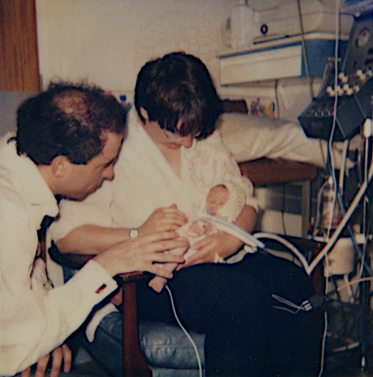 An old photograph shows two parents in hospital with their new baby, who is connected to lots of medical equipment.