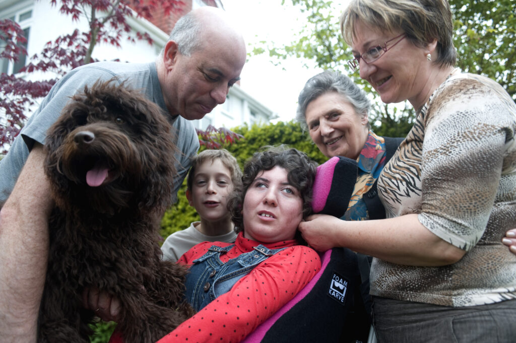 A young disabled woman is outside in her wheelchair, surrounded by her family, including the dog.