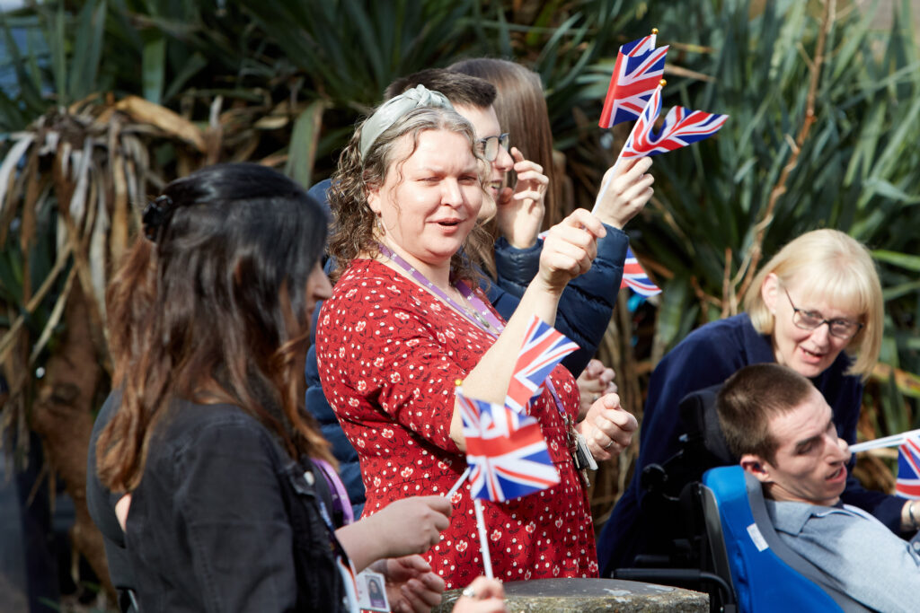 A group of people outdoors waving union jack flags.