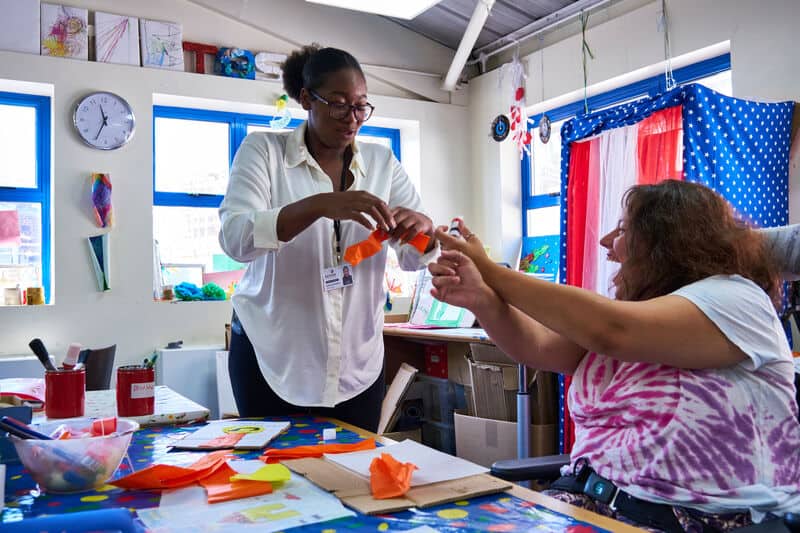 A woman assists another woman in an arts and crafts activity.