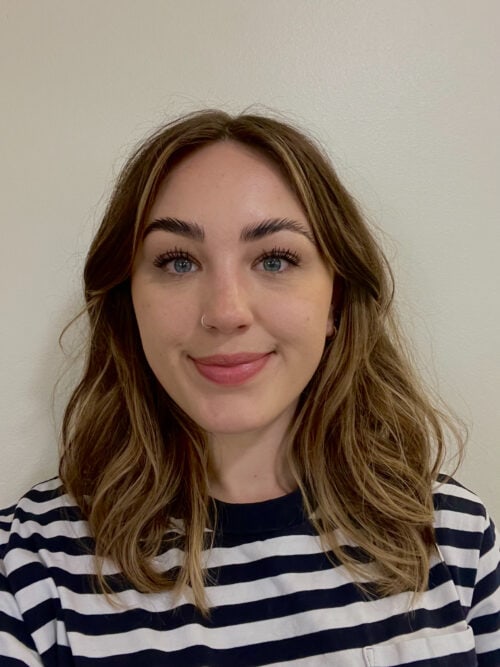 A girl with wavy light brown hair smiling to camera wearing a black and white striped tshirt.