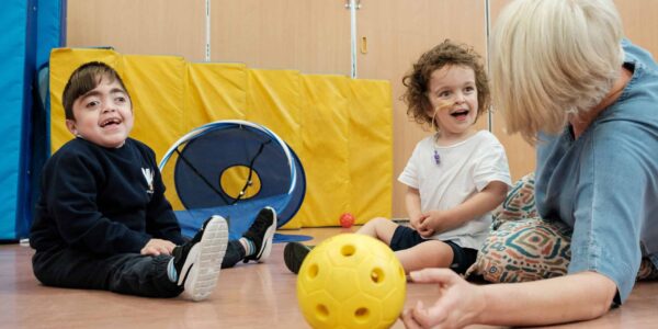 Amin and a friend, two small children, laughing as they play sensory football with an adult support worker.
