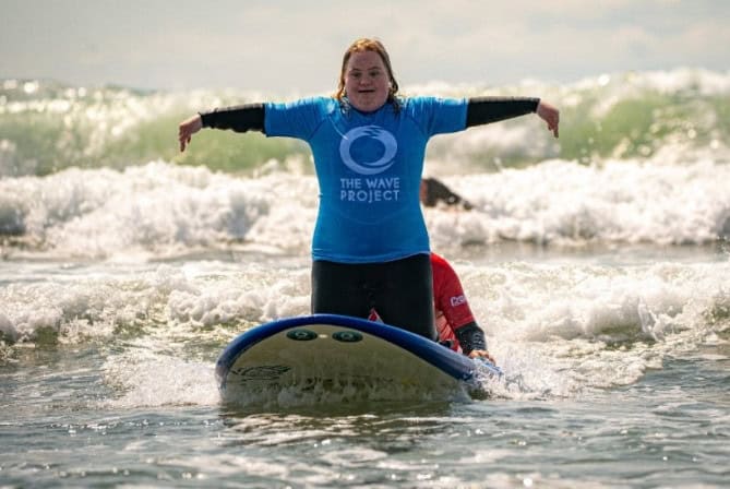 A woman wearing a blue shirt kneeling on a surfboard
