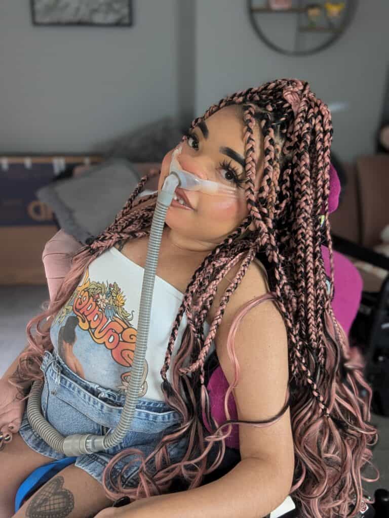 Shelby Lynch, a Black woman with long black and pink braids, sitting in a wheelchair.