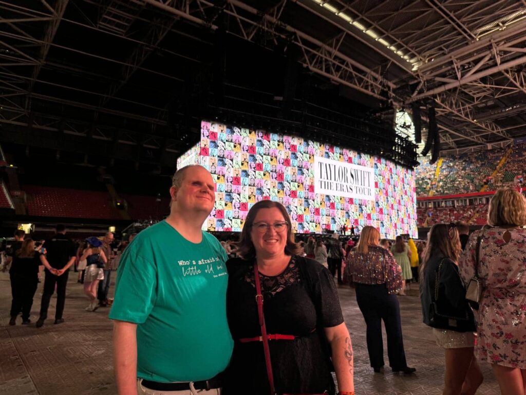 Steven posing with his wife in front of the big screen at Taylor Swift's Eras Tour show.