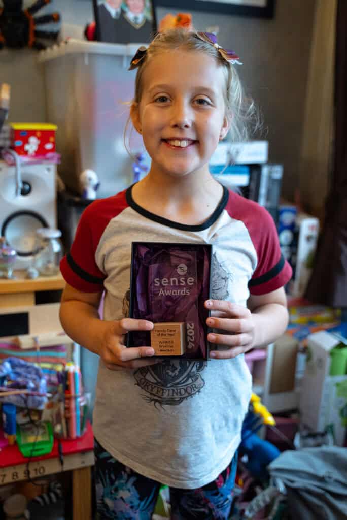 Bryanna is a young girl holding her Sense Award out in front of her.