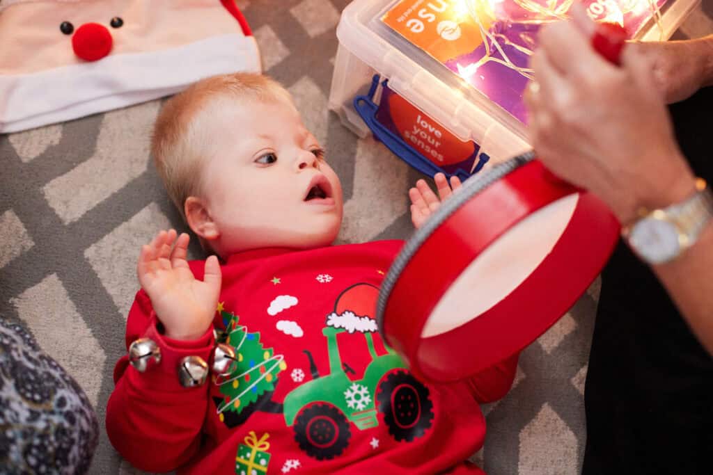 Arthur, a small boy wearing a Christmas jumper, looks with excitement at a handheld drum.