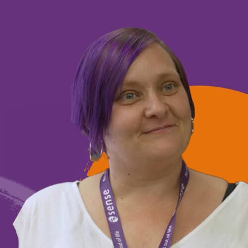 A woman with purple hair is smiling into the camera