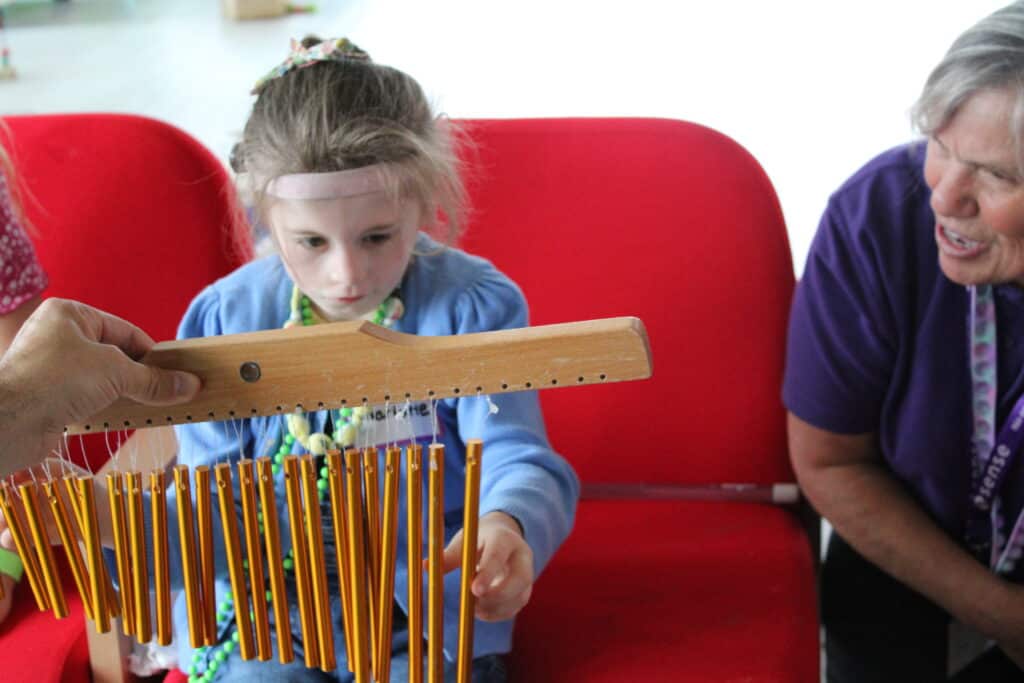 Charlotte playing with musical chimes, while a Sense support worker looks on.