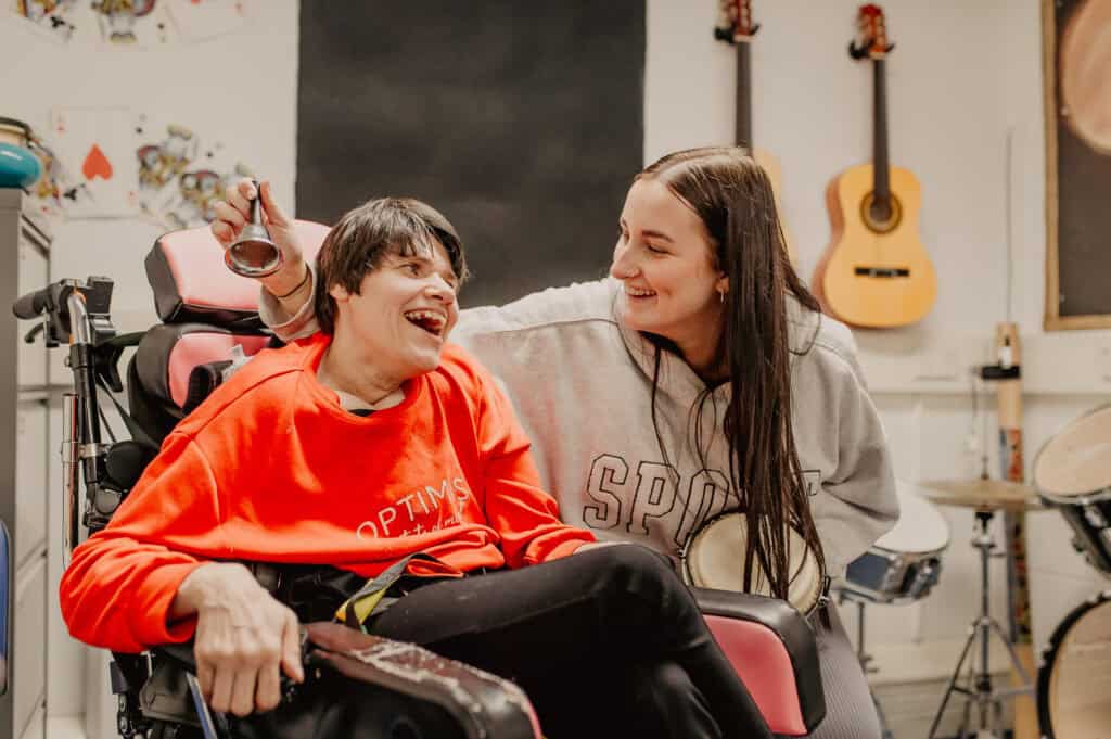 Two women smiling together in a music room, listening to the sound of a bell.