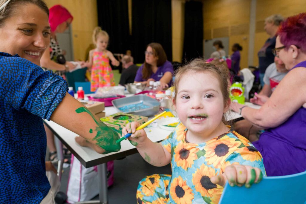 A little girl turns away from her painting to smile at the camera