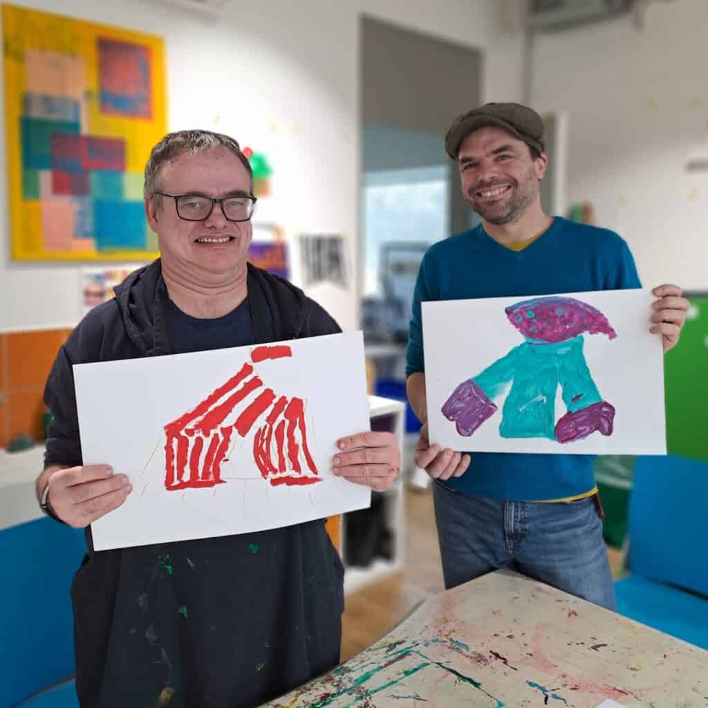 Two men holding up their paintings