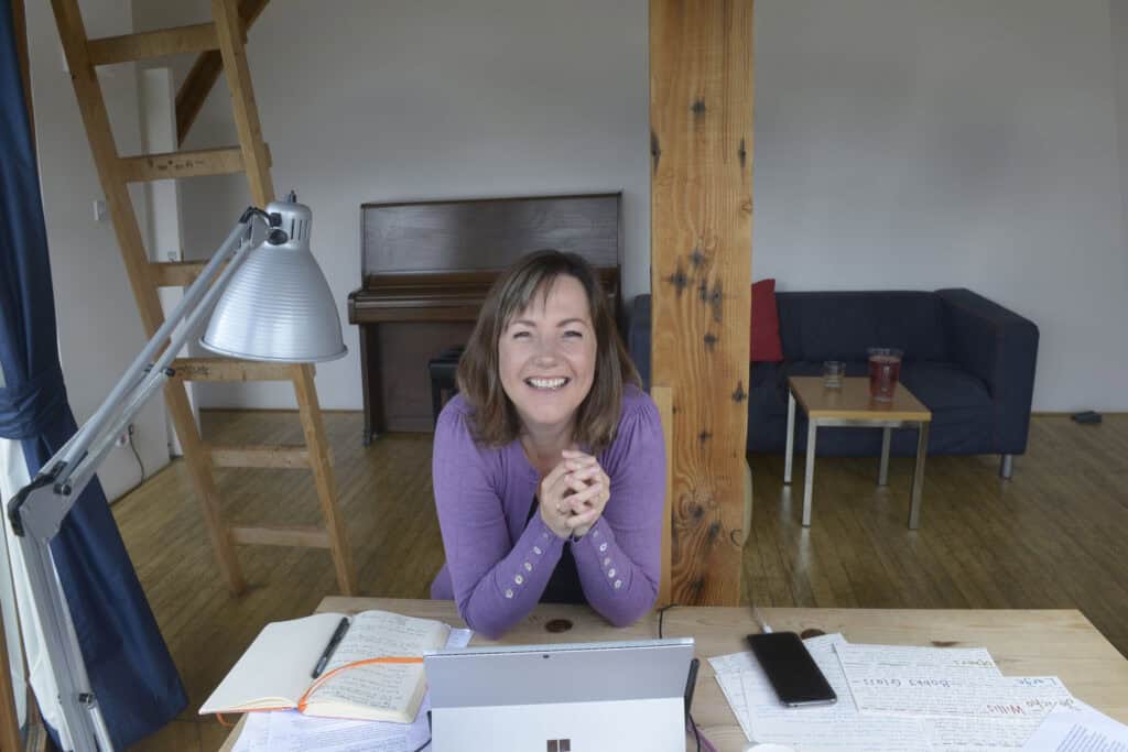 A woman sitting at a desk in a studio with papers spread out in front of her.
