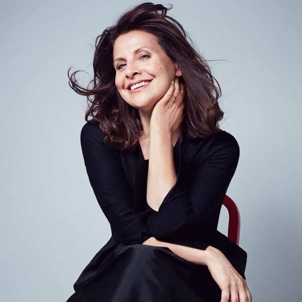 A woman wearing a black dress smiling and looking at the camera.