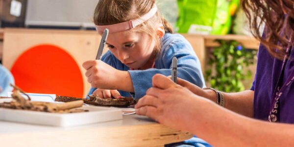 A young girl is leaning over a crafting table, she has a pen in her hand