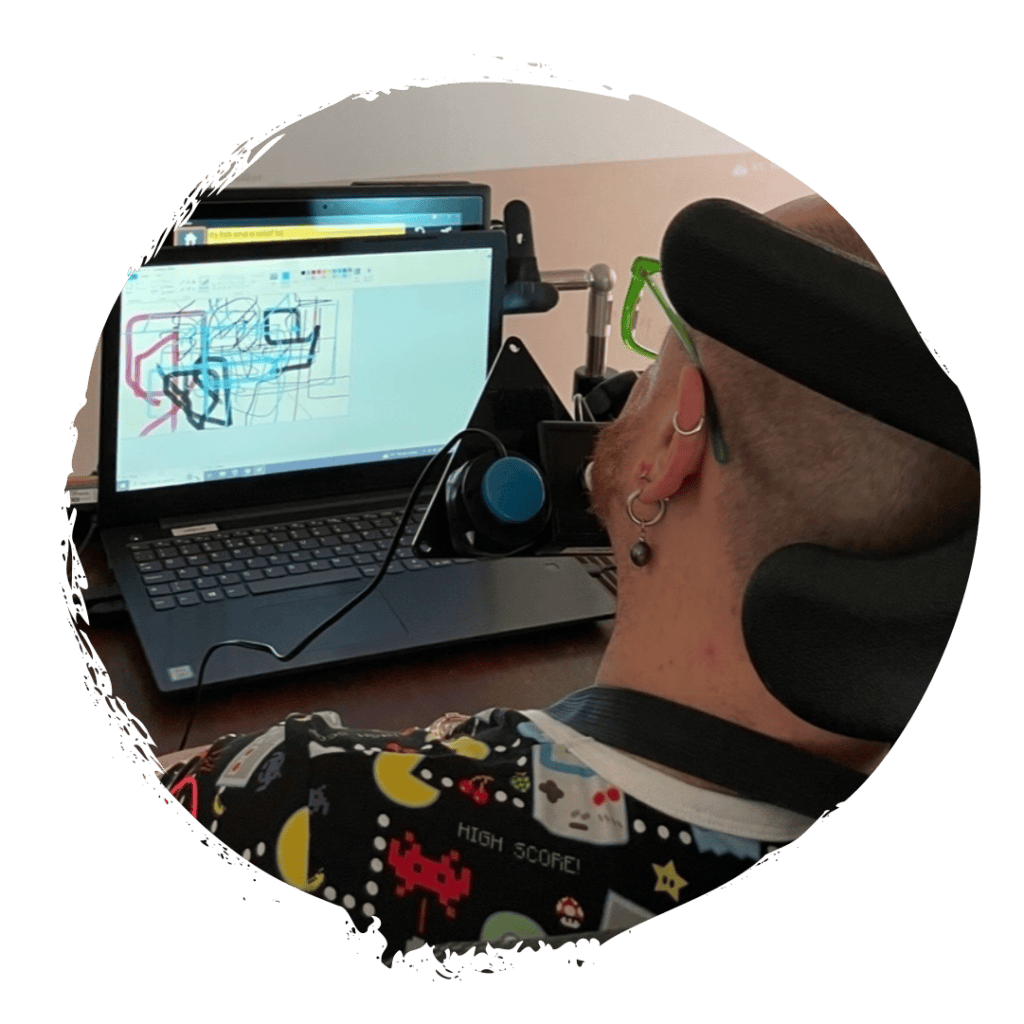Looking over a man's shoulder towards a laptop screen. The man is using assistive technology to draw on the screen.