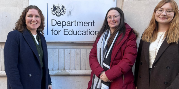Three women stand in front of the Department for Education sign