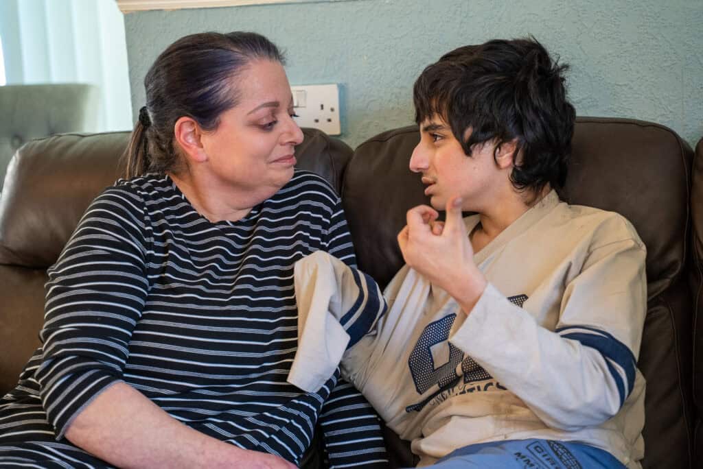 Sandra and Ayman are sitting facing each other. Ayman is using hand gestures to communicate with his mum