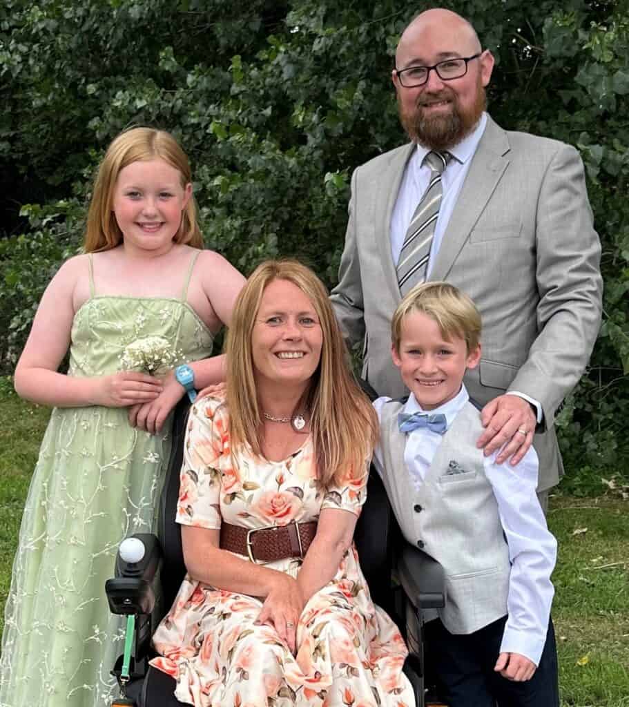 Steph and her family pose for a photograph. They are all dressed up smartly in dresses and suits and smiling very widely.