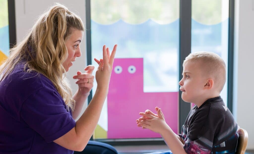 Thomas is sat opposite a member of the Sense Children's MSI team learning sign language.
