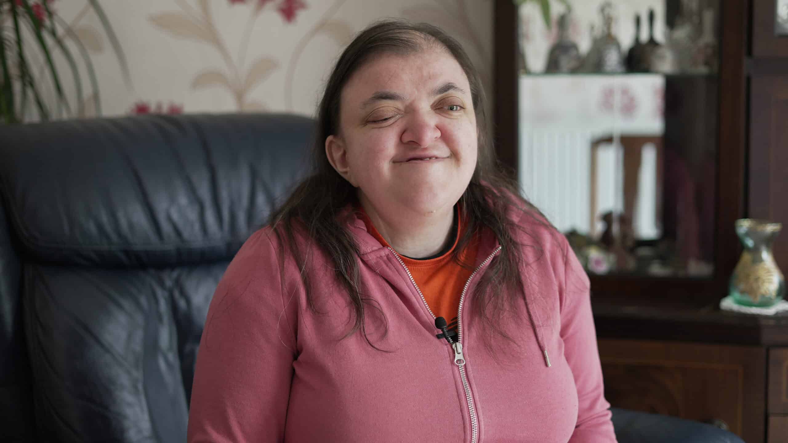A woman wearing a pink zipped top sitting on a sofa.