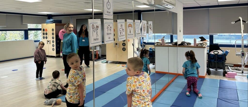 A wall is covered in mirrors, with children looking at their reflections. On the wall are Sign Language cards, showing how to communicate certain phrases.