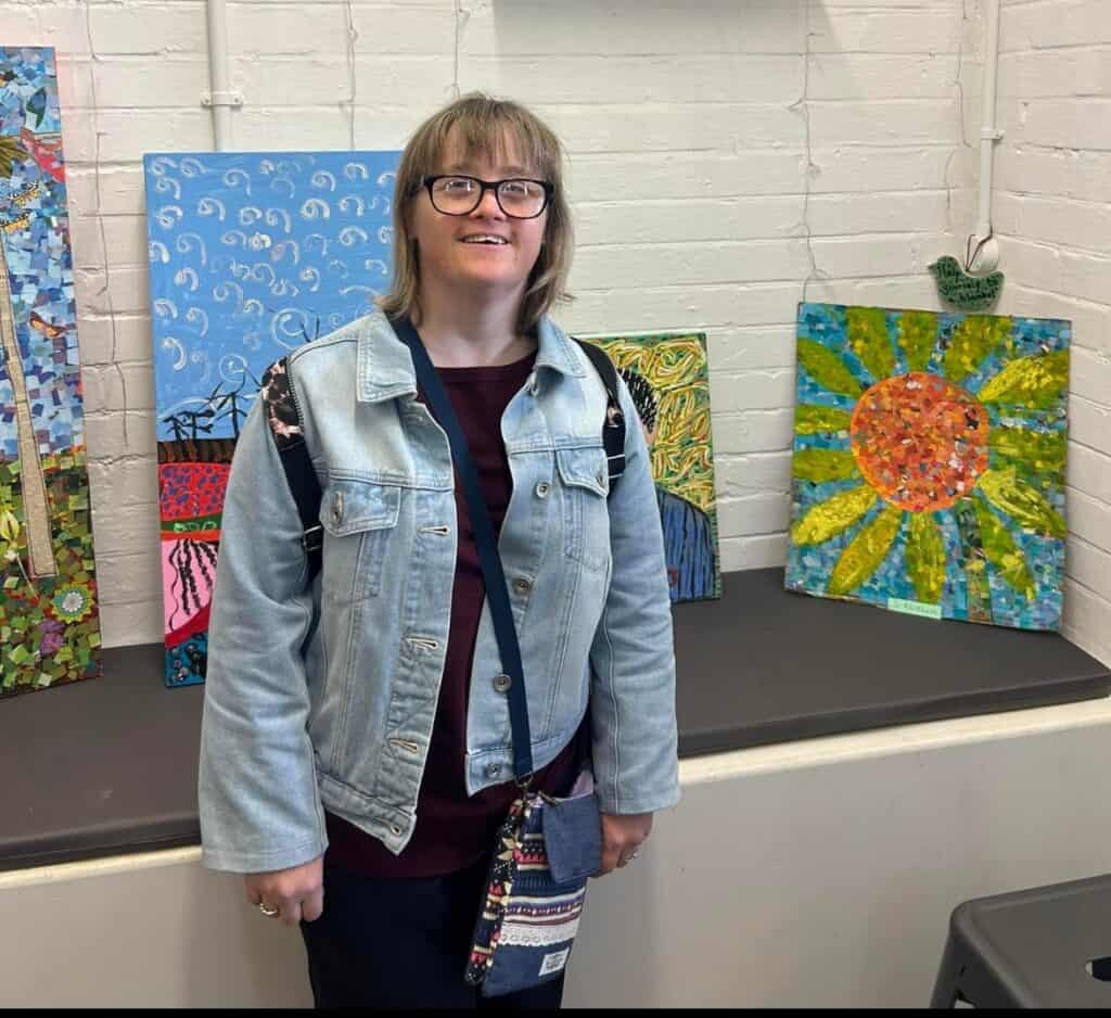 A woman wearing a denim jacket stading in front of a set of paintings.