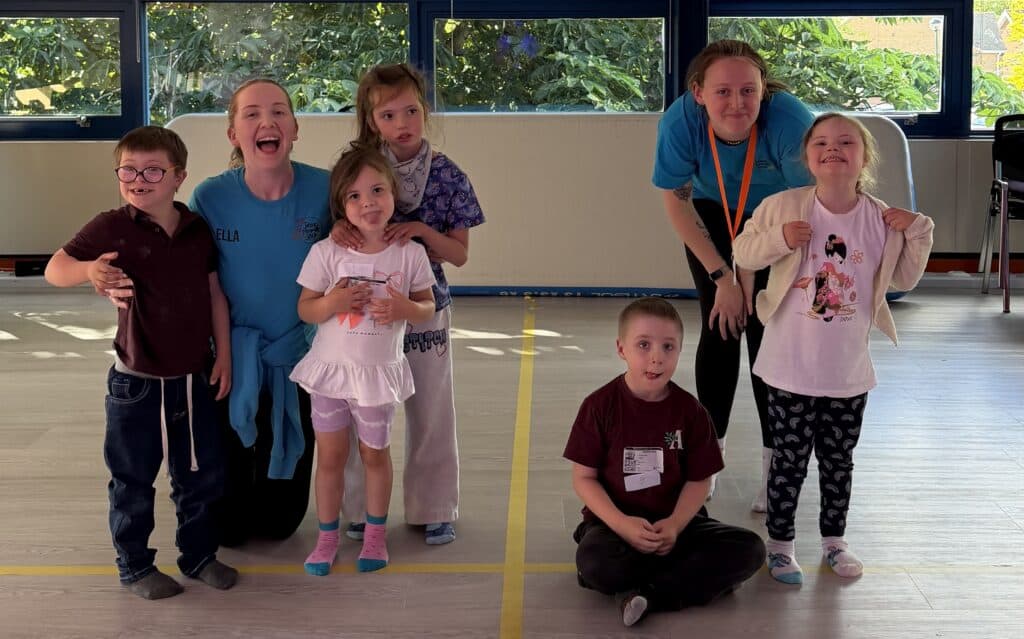 A group of children smiling widely after taking part in an activity, stood with their coaches.