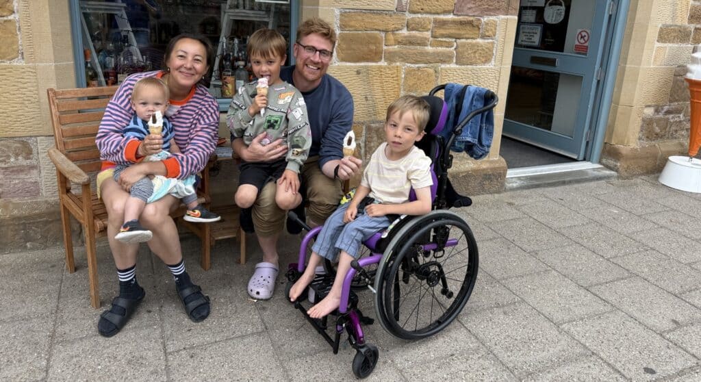 Five people are eating ice creams, smiling widely, in front of a shop window.